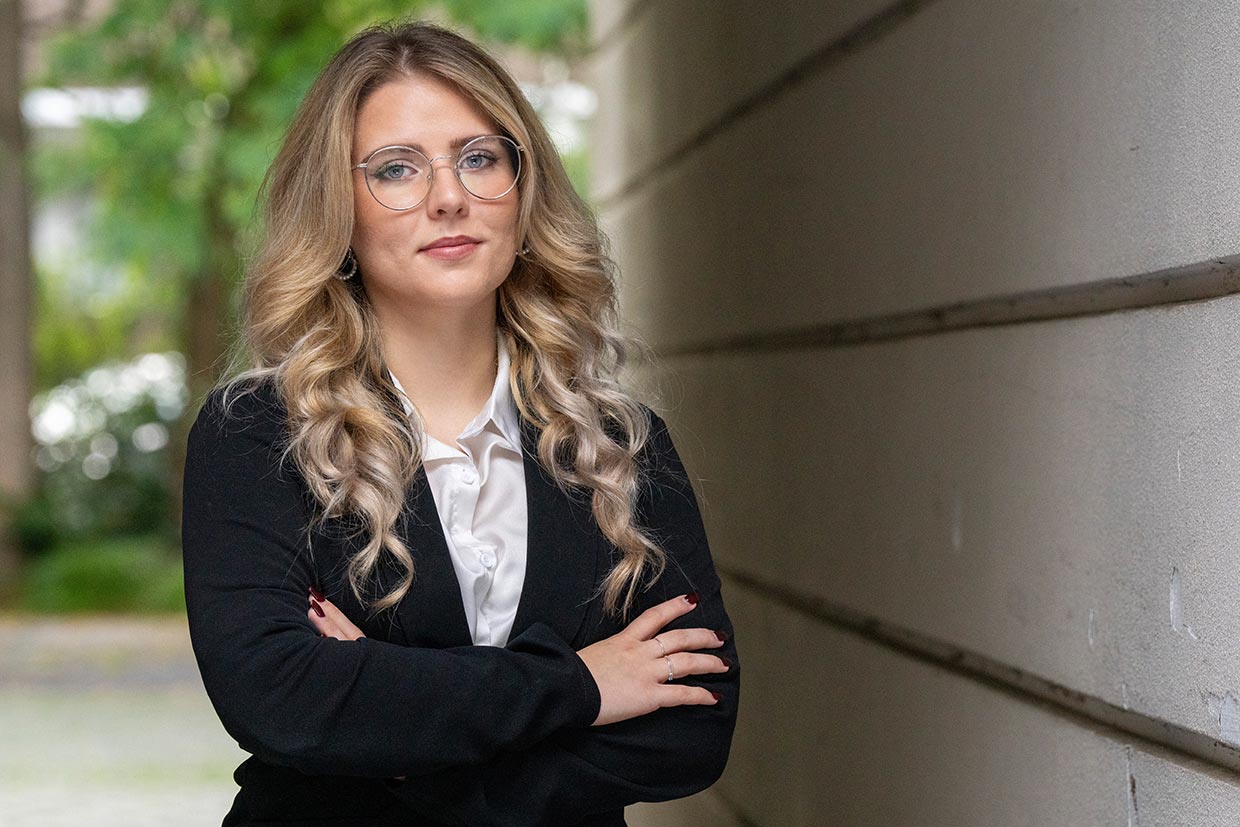 Junge Frau mit lockigem blondem Haar, Brille, seriösem Blick und schwarzem Blazer